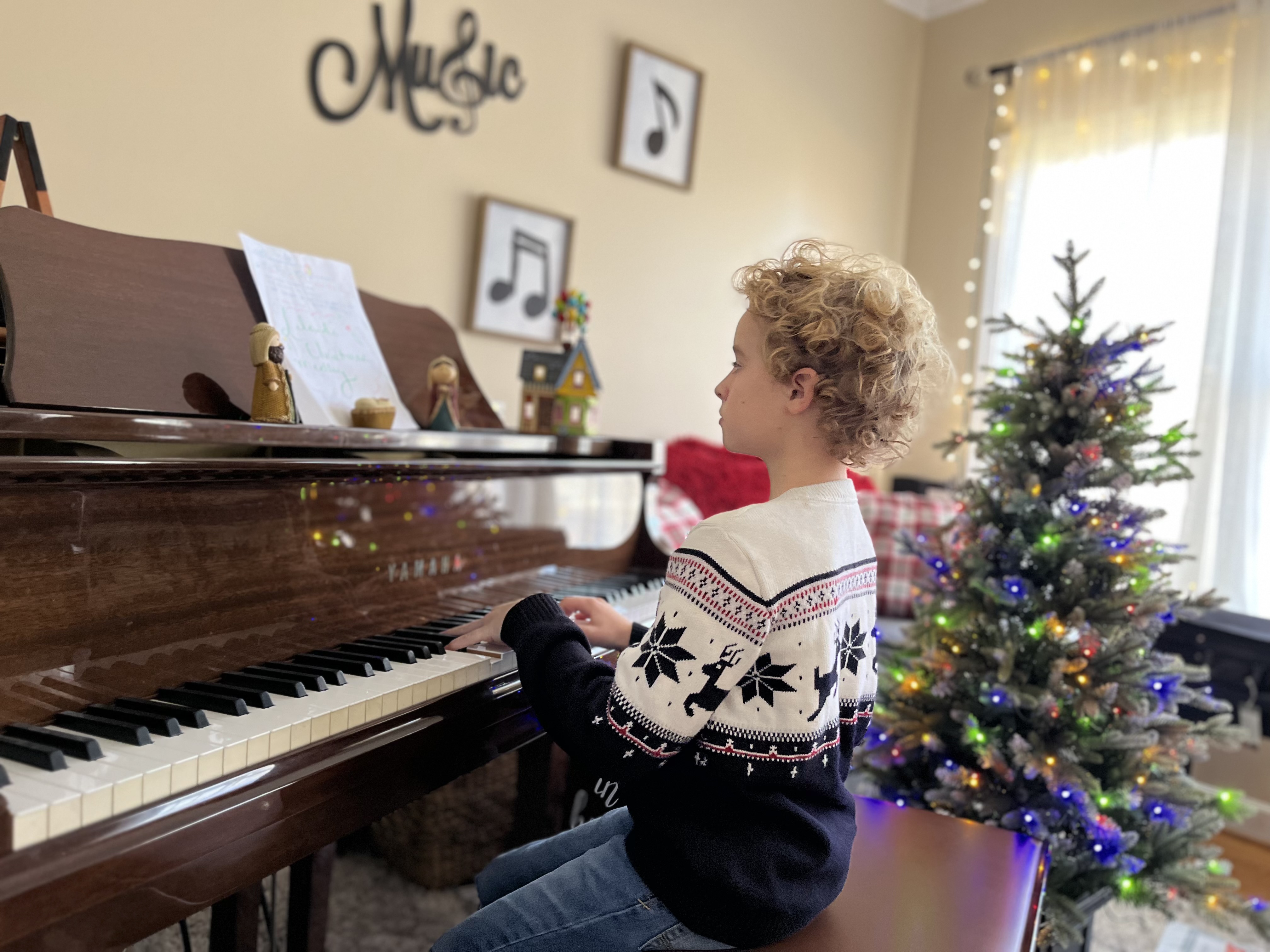 Leland playing a Yamaha upright piano beside a Christmas tree